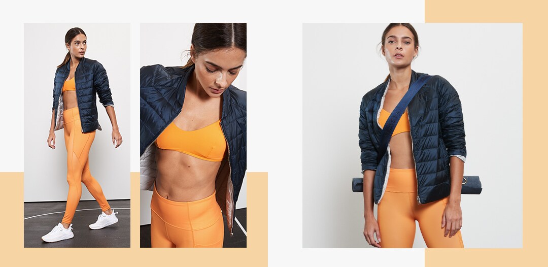 woman wearing all orange sports bra and tights and teal jacket over carrying a yoga mat
